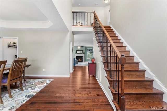 stairs with wood finished floors, baseboards, ceiling fan, and a lit fireplace