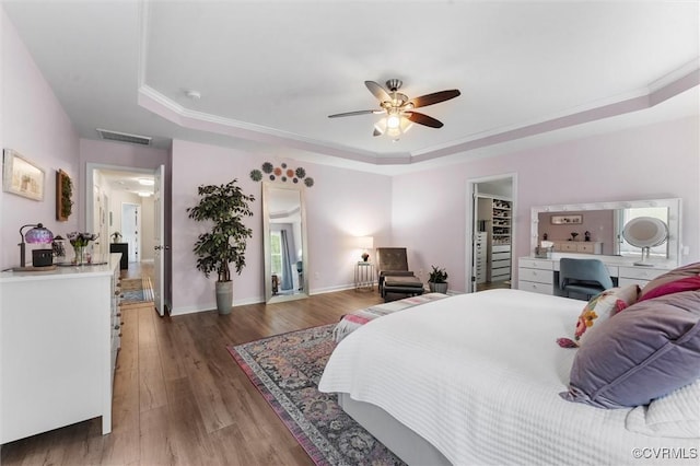 bedroom with a tray ceiling, wood finished floors, visible vents, crown molding, and baseboards