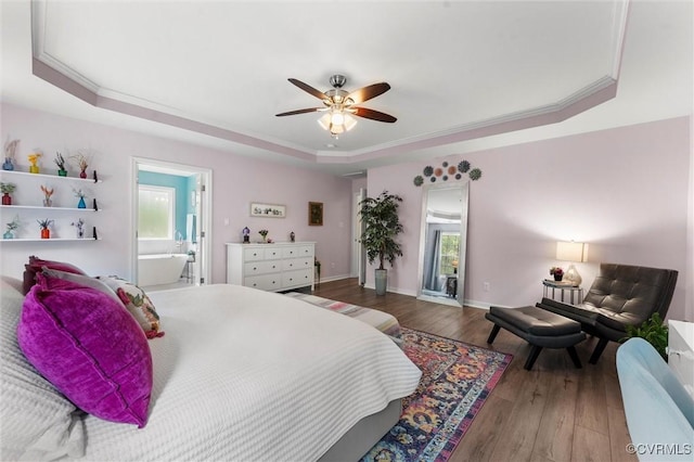 bedroom featuring wood-type flooring, a raised ceiling, multiple windows, and connected bathroom