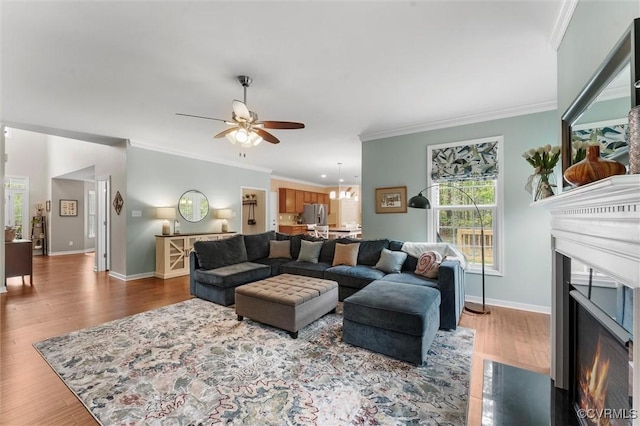 living area with a ceiling fan, wood finished floors, a fireplace with flush hearth, baseboards, and ornamental molding