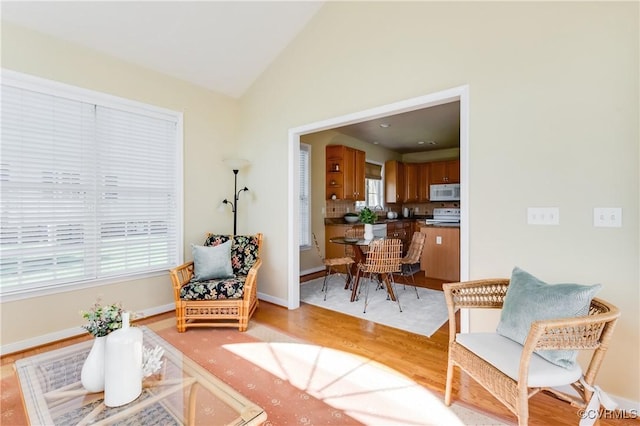 living area with vaulted ceiling, light wood finished floors, and baseboards