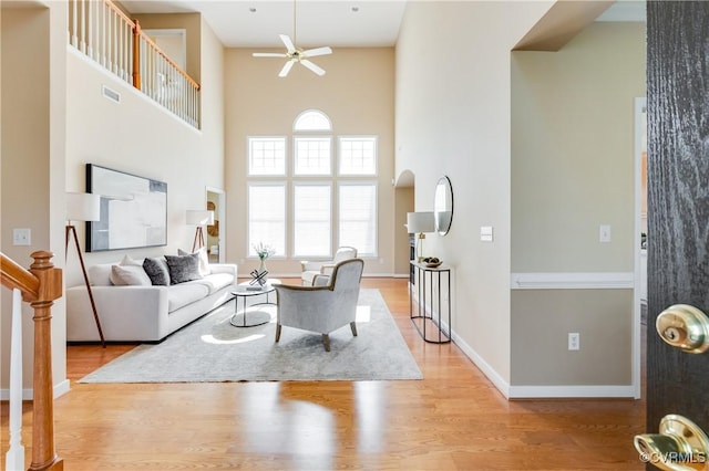 living room featuring wood finished floors, visible vents, a ceiling fan, and a towering ceiling
