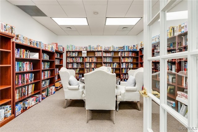 sitting room featuring carpet floors, wall of books, and a drop ceiling