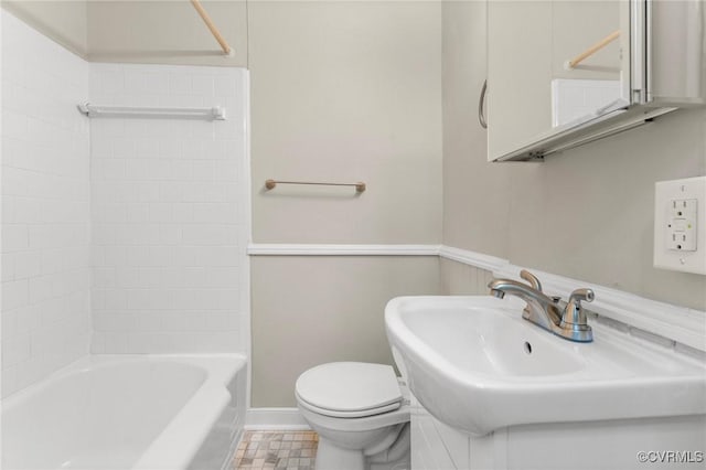 bathroom featuring toilet, washtub / shower combination, a sink, and baseboards