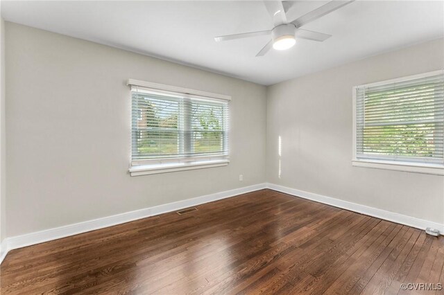 spare room with a wealth of natural light, a ceiling fan, dark wood-style floors, and baseboards