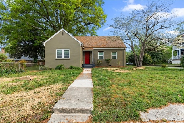 bungalow featuring fence, a shingled roof, a front yard, and stucco siding
