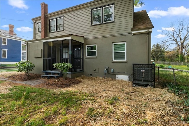 rear view of property featuring a chimney, a sunroom, fence, and stucco siding