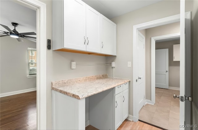 interior space featuring white cabinets, a ceiling fan, baseboards, and light stone counters
