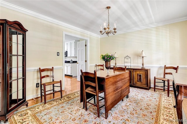 dining area featuring an inviting chandelier, a wainscoted wall, ornamental molding, and light wood-type flooring