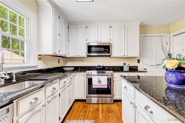 kitchen with a sink, light wood finished floors, dark stone counters, stainless steel appliances, and white cabinetry