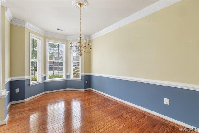 empty room featuring baseboards, an inviting chandelier, visible vents, crown molding, and hardwood / wood-style flooring