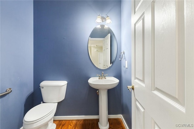 half bathroom featuring toilet, baseboards, a sink, and wood finished floors