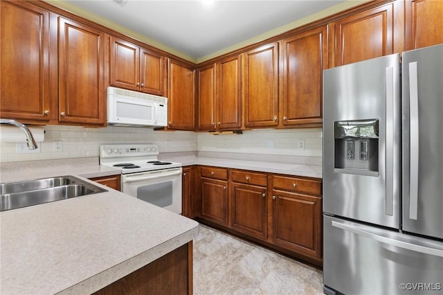 kitchen with light countertops, brown cabinetry, a sink, and white appliances