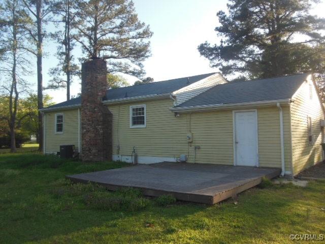 back of property with a wooden deck, a lawn, a chimney, and central AC