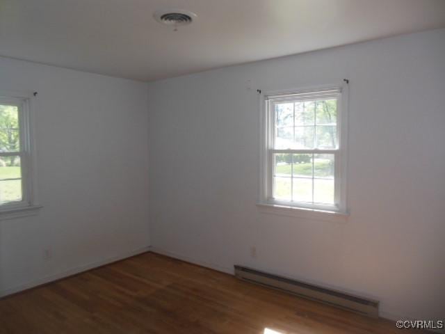 empty room with wood finished floors, visible vents, and baseboard heating