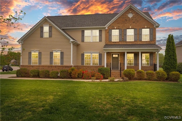 traditional home with brick siding, a yard, and covered porch