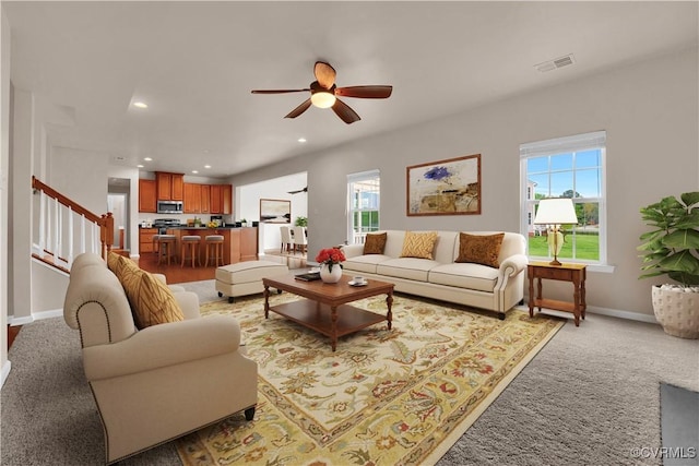 living room featuring stairs, a ceiling fan, recessed lighting, baseboards, and light colored carpet