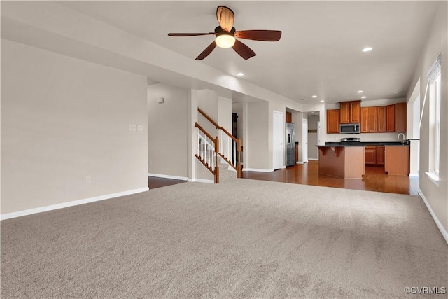 unfurnished living room featuring dark colored carpet, recessed lighting, stairs, ceiling fan, and baseboards