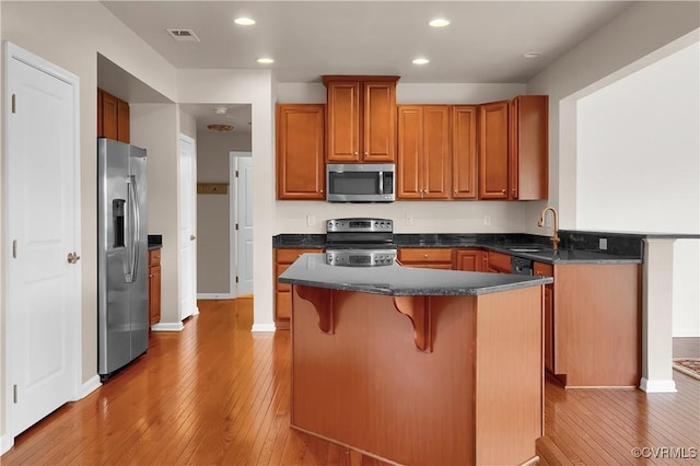 kitchen with appliances with stainless steel finishes, a sink, light wood-type flooring, dark countertops, and a kitchen breakfast bar