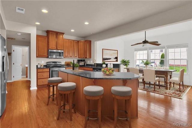 kitchen with appliances with stainless steel finishes, brown cabinets, a center island, light wood finished floors, and a kitchen breakfast bar