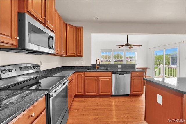 kitchen featuring appliances with stainless steel finishes, a sink, light wood-style floors, a peninsula, and brown cabinets