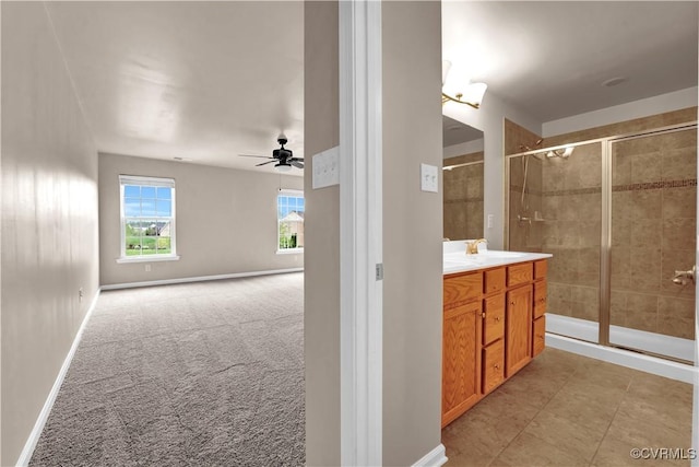 full bathroom featuring ceiling fan, a stall shower, double vanity, and baseboards