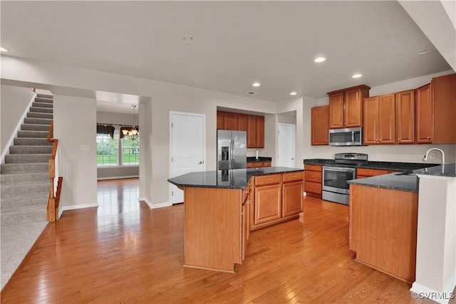kitchen with stainless steel appliances, a sink, a center island, light wood-type flooring, and a chandelier