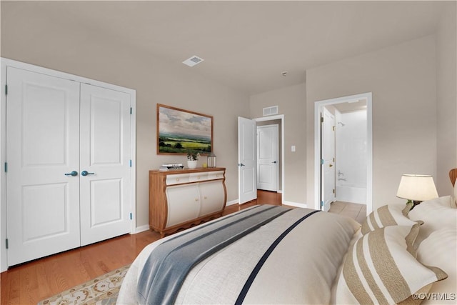bedroom with wood finished floors, baseboards, a closet, and ensuite bath
