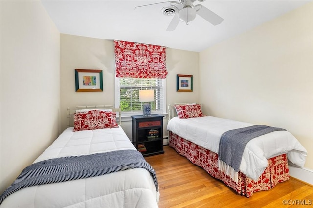bedroom with a ceiling fan, a baseboard heating unit, and light wood-style floors
