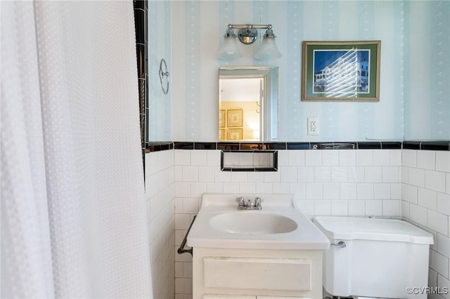 bathroom featuring tile walls, vanity, wallpapered walls, and toilet