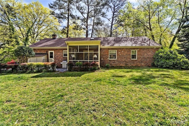 rear view of property featuring brick siding, a lawn, a chimney, and a sunroom