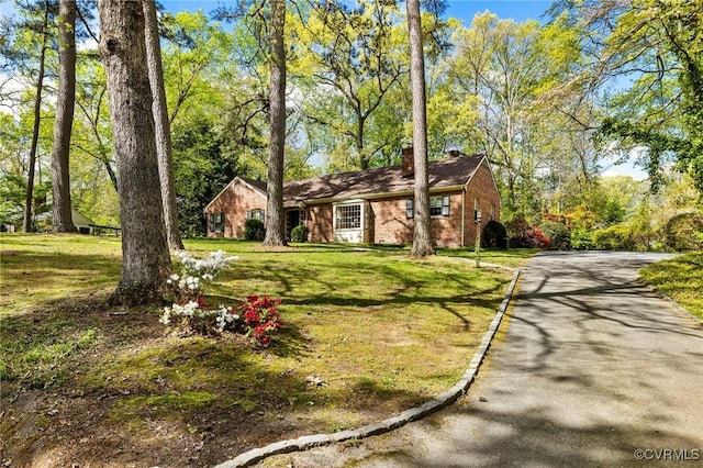 ranch-style home with a chimney, driveway, a front lawn, and brick siding
