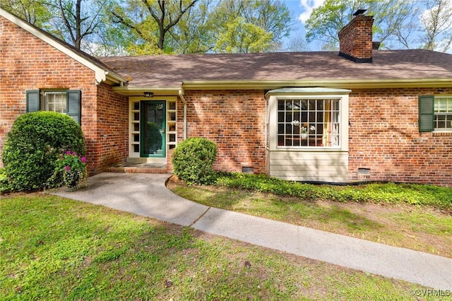 doorway to property with a lawn, brick siding, a chimney, and roof with shingles