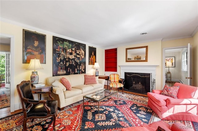 living area with crown molding, a fireplace, built in shelves, wood finished floors, and visible vents