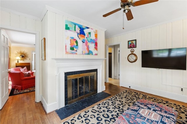 living room featuring wood-type flooring, ornamental molding, and a fireplace with flush hearth