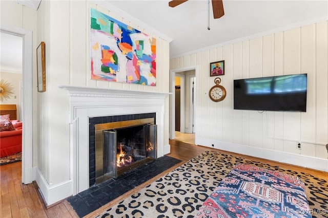 living room featuring a fireplace with flush hearth, baseboards, ornamental molding, and hardwood / wood-style flooring