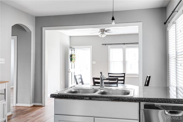 kitchen with ceiling fan, arched walkways, a sink, light wood finished floors, and dishwasher