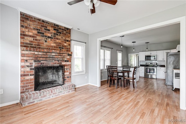 living room featuring a ceiling fan, baseboards, light wood finished floors, and a fireplace
