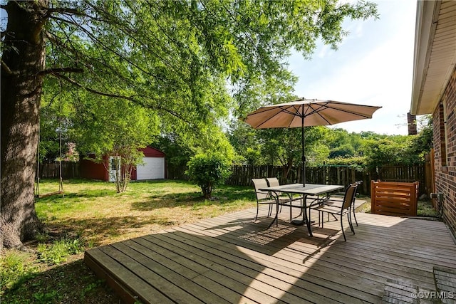 deck with outdoor dining area, a fenced backyard, and a yard
