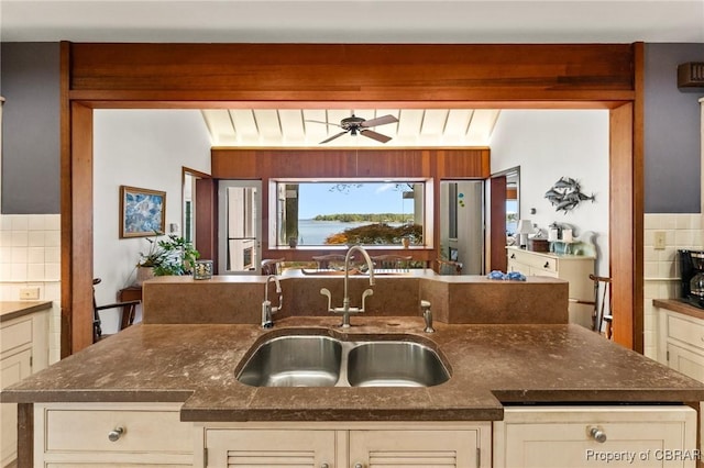 kitchen with decorative backsplash, a sink, dark stone counters, and ceiling fan