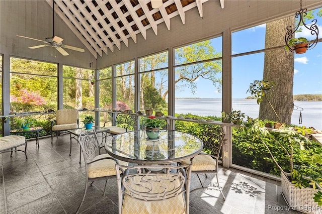 sunroom featuring a ceiling fan, outdoor dining area, and a water view