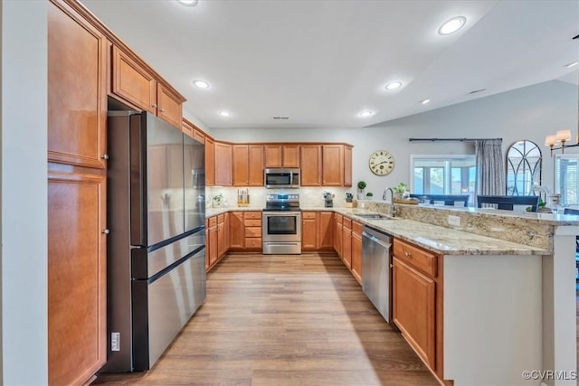 kitchen with appliances with stainless steel finishes, light stone counters, a sink, a peninsula, and light wood-type flooring