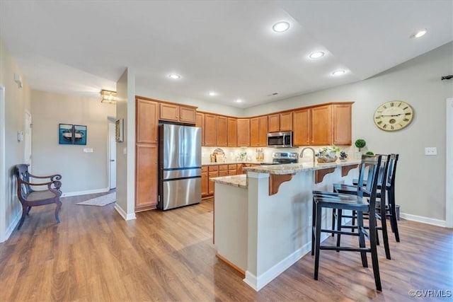 kitchen with a peninsula, a breakfast bar, light stone countertops, light wood-style flooring, and stainless steel appliances