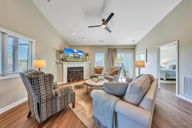 living area with ceiling fan, visible vents, a fireplace with flush hearth, wood finished floors, and baseboards
