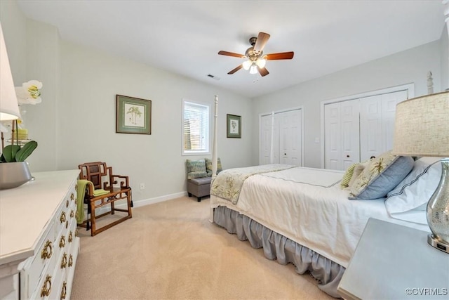 bedroom featuring light colored carpet, two closets, a ceiling fan, baseboards, and visible vents