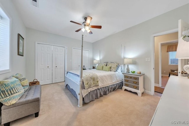 bedroom featuring a ceiling fan, baseboards, light carpet, and two closets