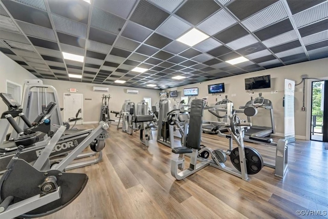 exercise room with baseboards, a wall unit AC, and wood finished floors