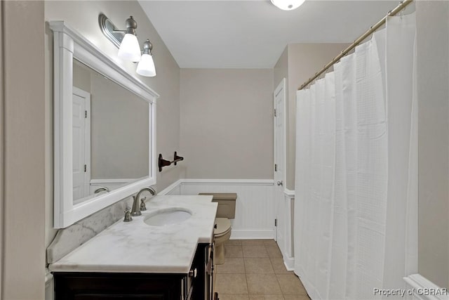 bathroom with tile patterned flooring, vanity, a wainscoted wall, and toilet