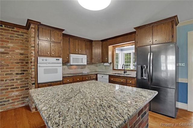 kitchen featuring light wood-style flooring, a sink, white appliances, light stone countertops, and a kitchen island