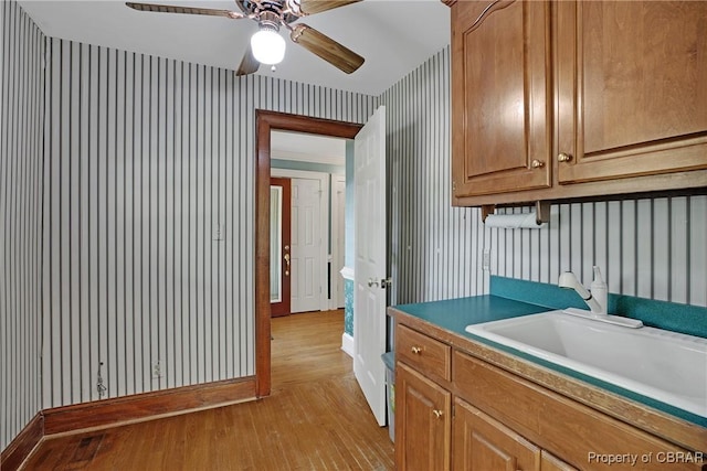 kitchen featuring a sink, baseboards, light wood-style floors, wallpapered walls, and a ceiling fan